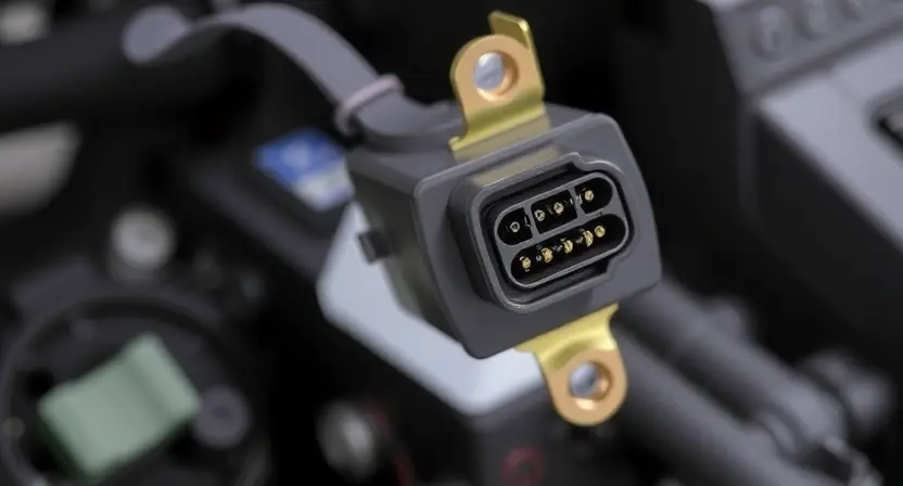 A close-up photograph of an ABS solenoid valve with a visible wiring harness. The focus should be on the solenoid coil and its connection points. The background should be blurred, suggesting an automotive interior. The image should clearly show the physical components of the solenoid and its electrical connections.