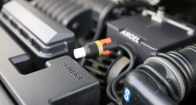 A close-up of a car's engine bay, focusing on the coolant temperature sensor and its wiring. The engine should be clean and well-maintained. The background should be slightly blurred to emphasize the sensor.