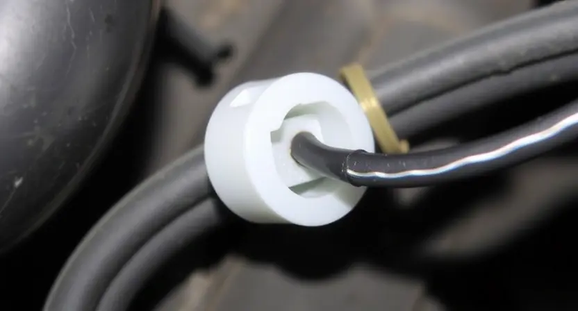A close-up shot of an automotive wiring harness with a damaged or frayed wire near a sensor connector. The sensor should be partially visible, showing its circular shape and mounting. Focus on the wire and the damaged area, highlighting the low signal issue.